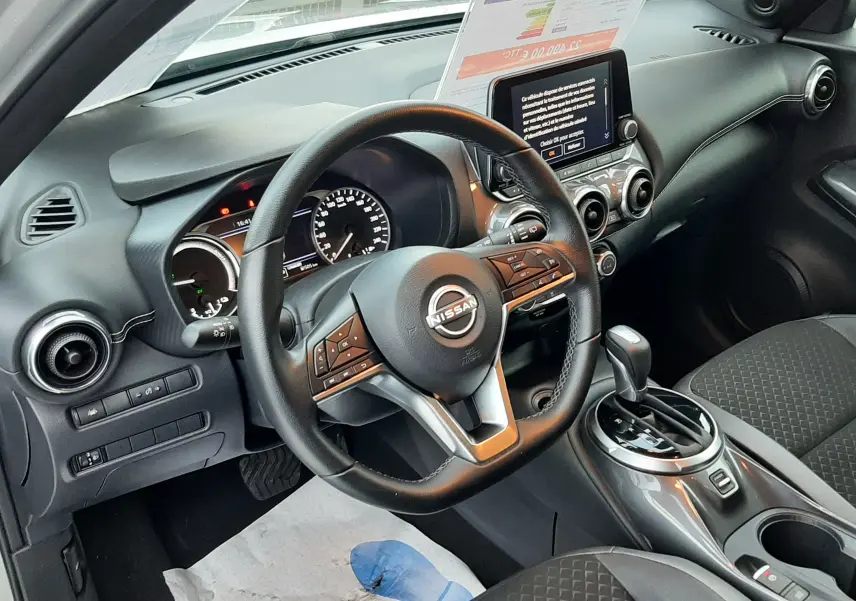 Vue intérieure côté conducteur du Nissan Juke 2024, mettant en valeur le volant multifonction et la console centrale moderne.