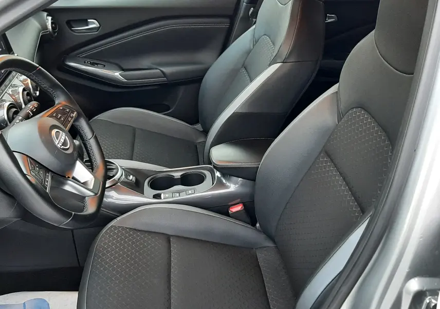 Intérieur du Nissan Juke 2024 gris perle métal, vue côté conducteur, sièges noirs avec surpiqûres et console centrale.