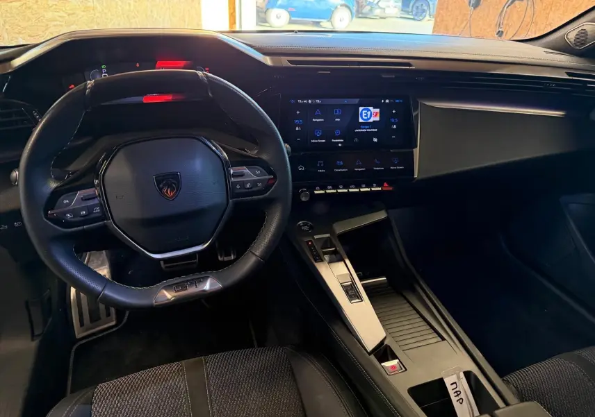 Vue intérieure de la Peugeot 408 GT 2025, tableau de bord noir avec volant compact et écran tactile central lumineux.