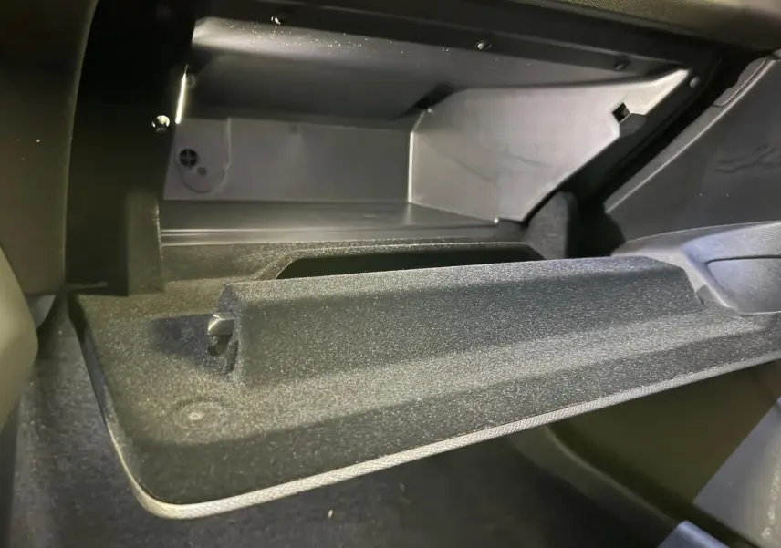 Gros plan sur la boîte à gants ouverte de la Peugeot 408 gris, montrant l'intérieur spacieux et les finitions textiles.