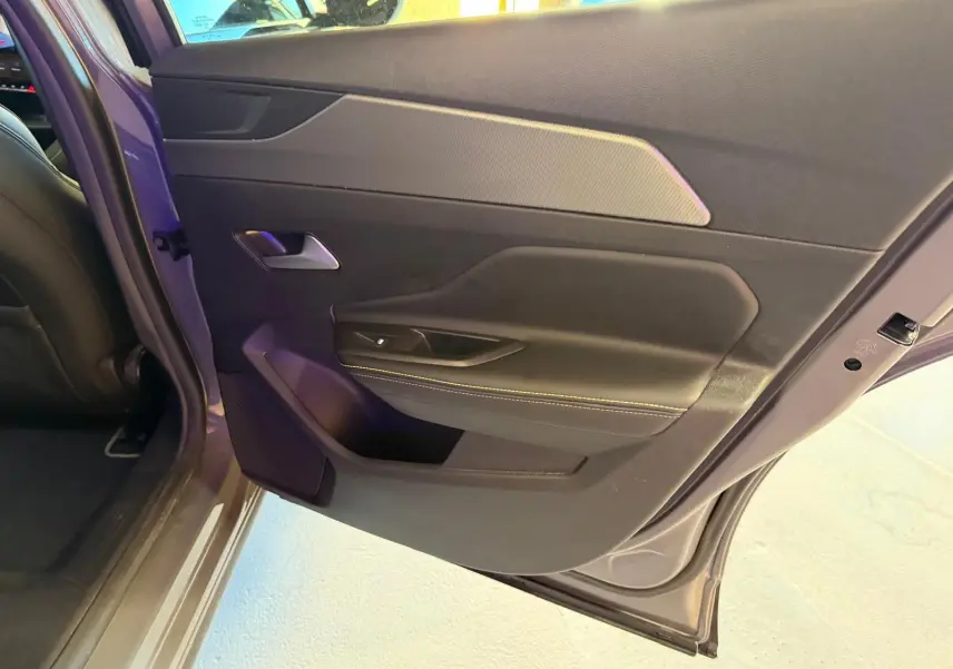 Vue rapprochée de la porte arrière gauche grise du Peugeot 408 2025 avec surpiqûres vertes et poignée argentée.