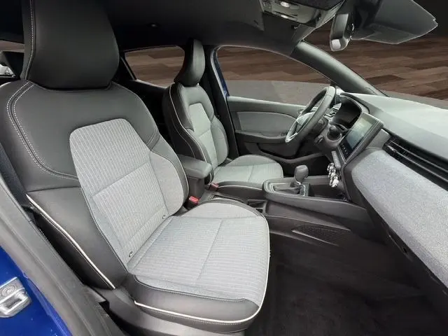 Vue intérieure côté gauche de la Renault Clio Techno E-Tech 2025, sièges gris et noir avec tableau de bord moderne.