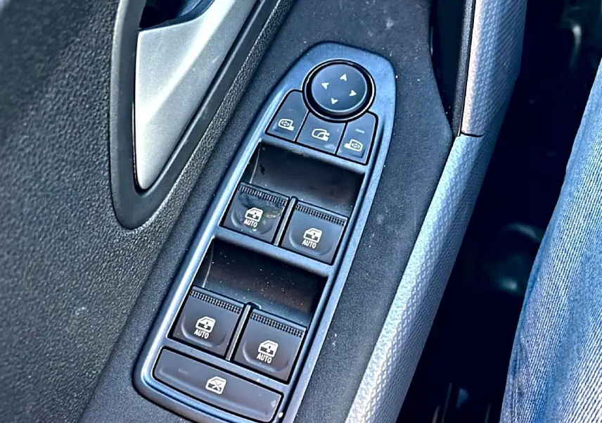 Gros plan sur les commandes des vitres électriques et rétroviseurs sur la porte côté gauche d’un Dacia Duster noir.