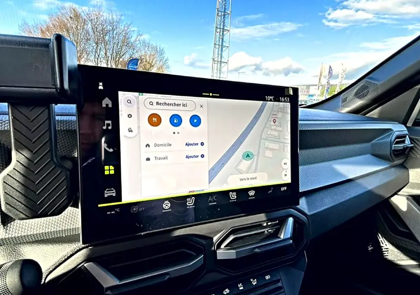 Vue intérieure du tableau de bord du Dacia Duster 2026 avec écran tactile GPS et commandes climatisation visibles.