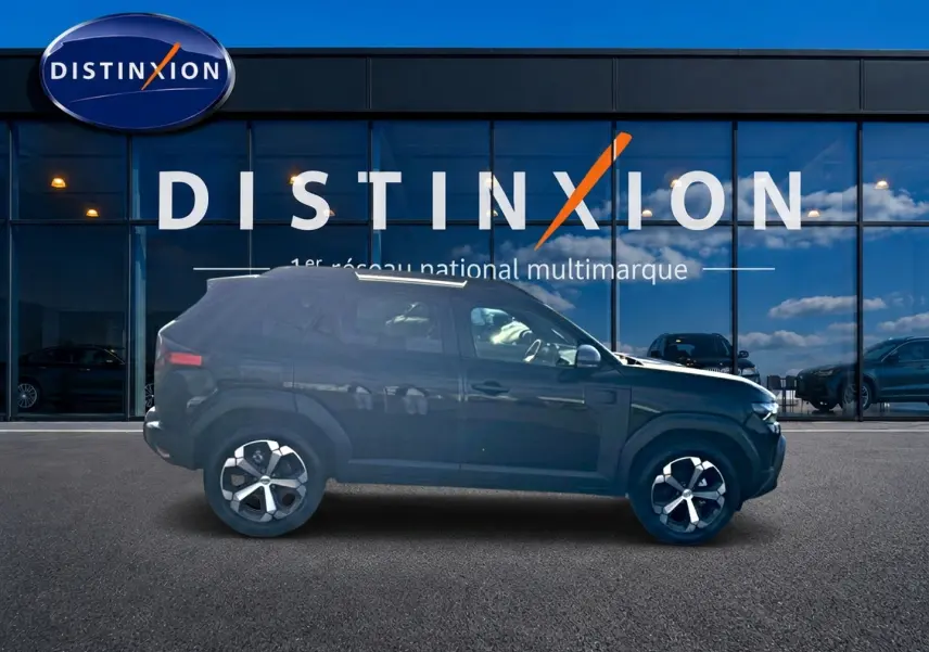 Vue de profil côté gauche d'un Dacia Duster noir 2026 garé devant une vitrine avec logo Distinxion.