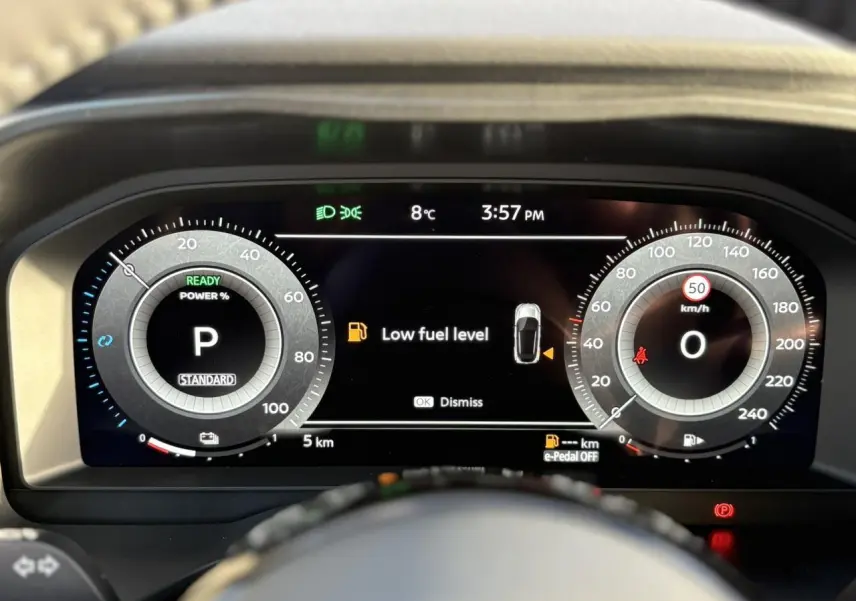 Vue rapprochée du combiné d'instrumentation numérique du Nissan Qashqai noir, affichant un avertissement de faible carburant.