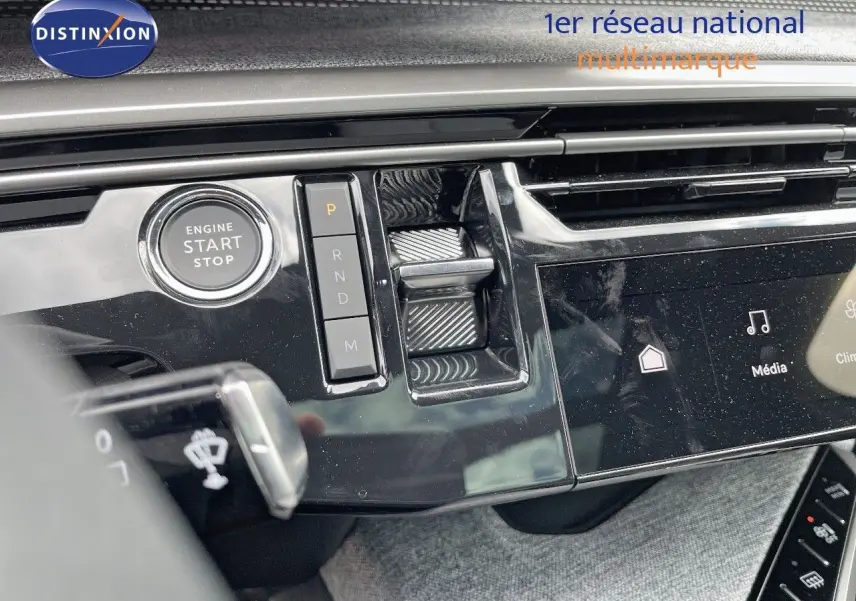 Gros plan sur la console centrale noire brillante du Peugeot 5008 Hybrid 2025 avec bouton start/stop et commandes de boîte automatique.