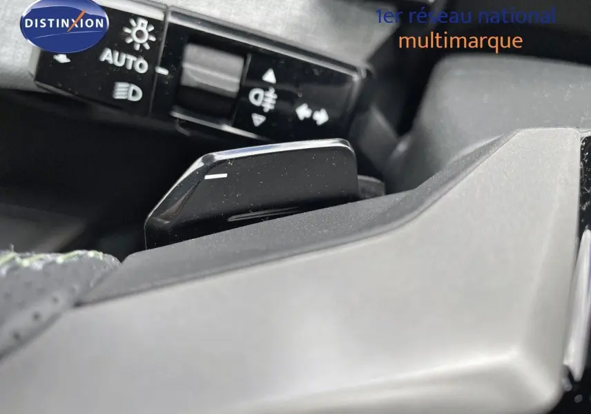 Gros plan sur la palette de changement de vitesse noire du Peugeot 5008 Hybrid 2025, avec commandes d'éclairage en arrière-plan.