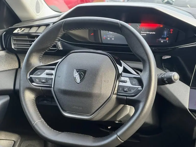 Vue rapprochée du volant multifonction noir de la Peugeot 308 2024 avec tableau de bord numérique en arrière-plan.