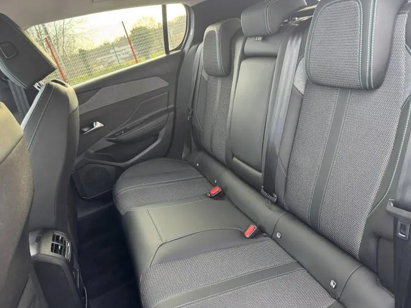 Vue intérieure côté arrière droit montrant les sièges arrière en tissu et cuir noir avec surpiqûres contrastantes du Peugeot 308 2024.