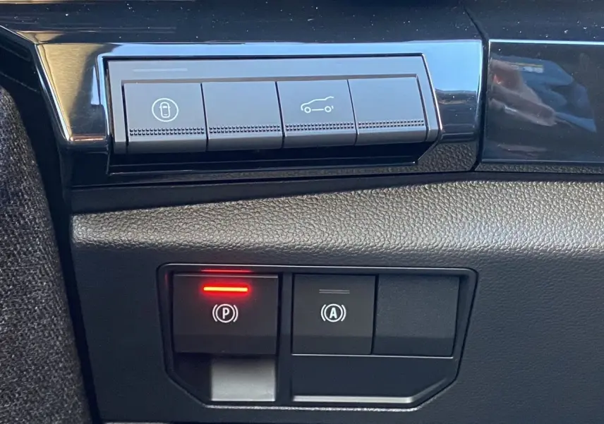 Gros plan sur les commandes noires du tableau de bord du Renault Espace, avec témoin rouge actif sur frein de parking.