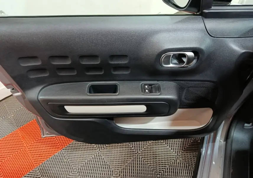 Vue rapprochée de la porte avant gauche gris clair de la Citroën C3 avec poignée intérieure et commandes de vitres.