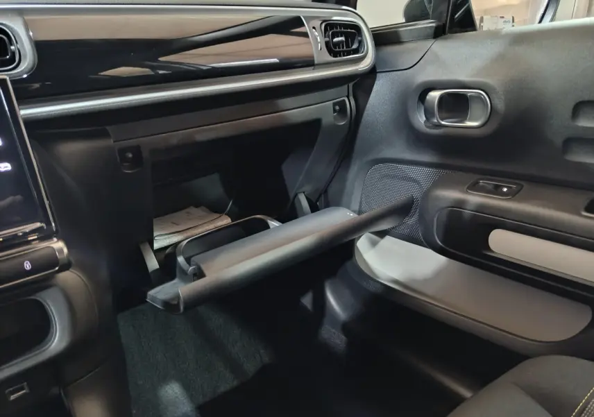 Intérieur de la Citroën C3 2024 gris clair, vue côté passager avec boîte à gants ouverte et tableau de bord noir brillant.