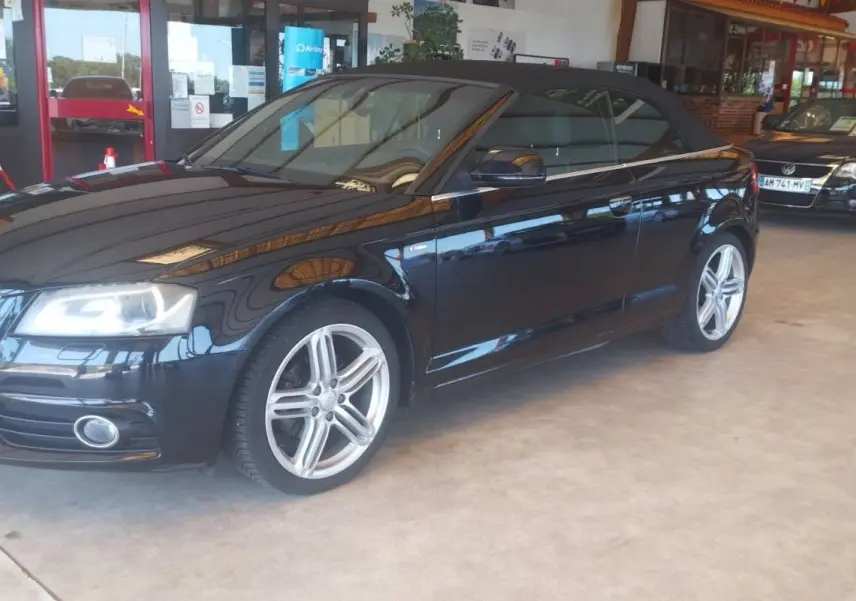 Audi A3 Cabriolet noir vue 3/4 avant droit avec capote fermée, jantes alliage et intérieur sombre en showroom.