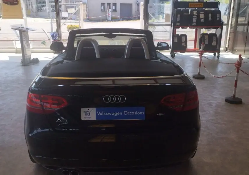 Vue arrière d'une Audi A3 Cabriolet noire 2010 avec capote ouverte, exposée en intérieur dans un showroom.