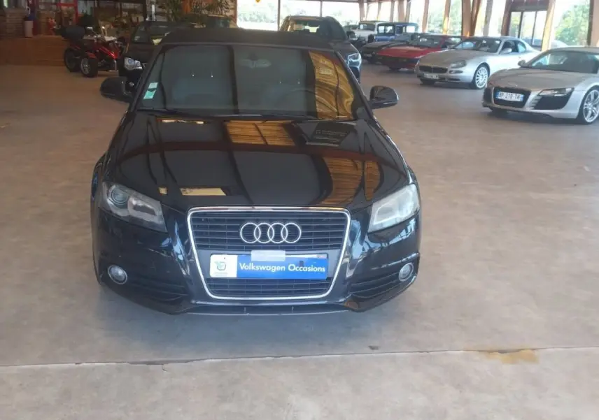 Audi A3 Cabriolet noir vue de face dans un showroom, mettant en valeur sa calandre et ses phares distinctifs.
