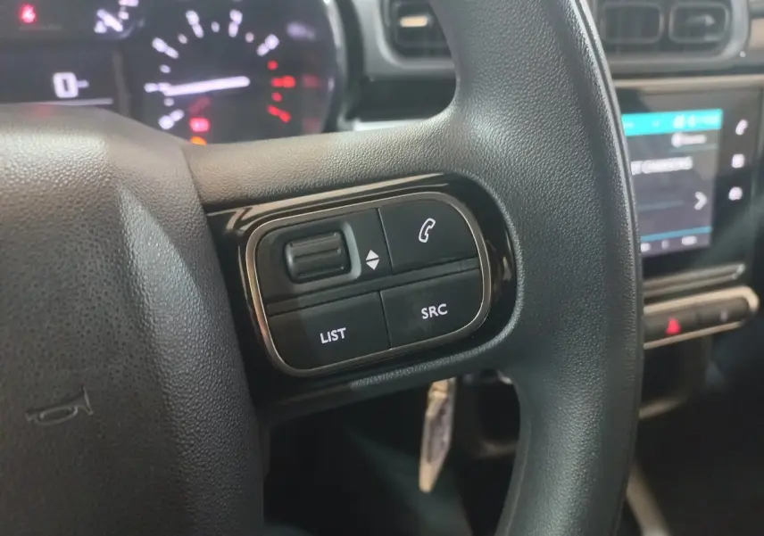 Gros plan sur les commandes gauche du volant noir de la Citroën C3 2024 avec tableau de bord et écran tactile en arrière-plan.