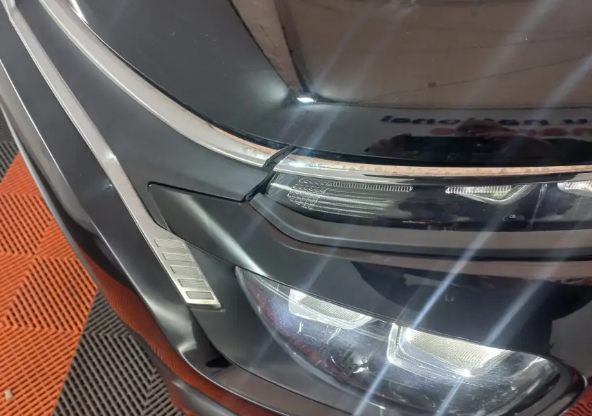 Gros plan sur le phare avant gauche noir brillant de la Citroën C3 2024 avec détails chromés et LED allumées.