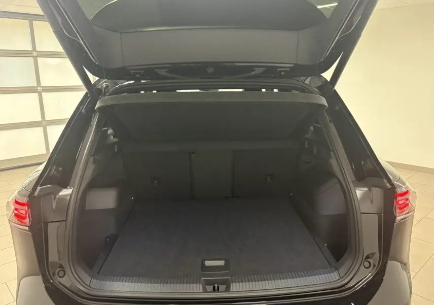 Coffre ouvert vu de l'arrière d'un Volkswagen Tiguan 2025 noir intense nacré avec hayon et intérieur de coffre spacieux.