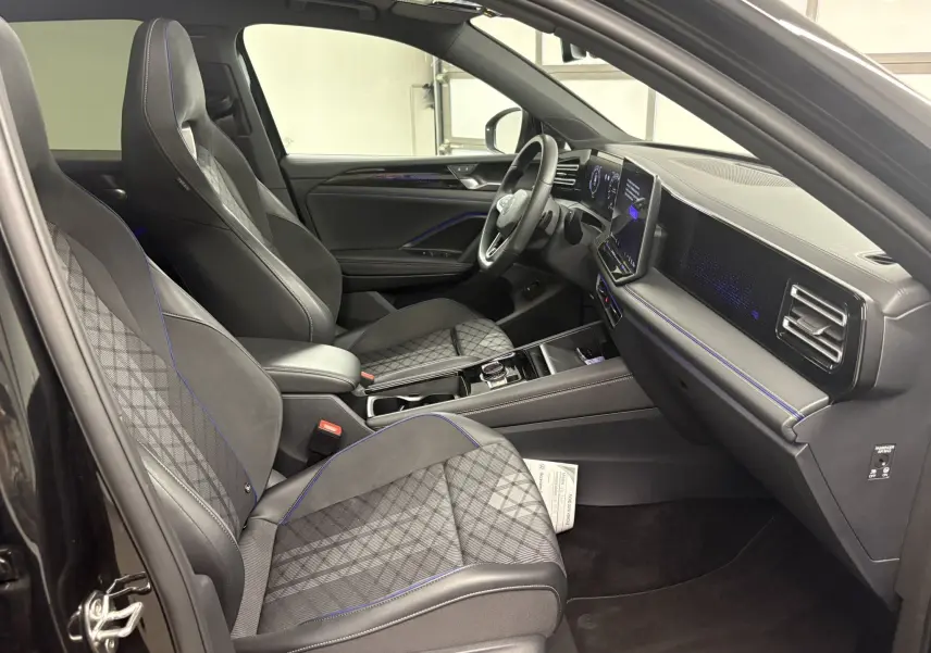 Vue intérieure côté conducteur du Volkswagen Tiguan 2025 noir intense nacré, sièges sport avec surpiqûres bleues et tableau de bord digital.