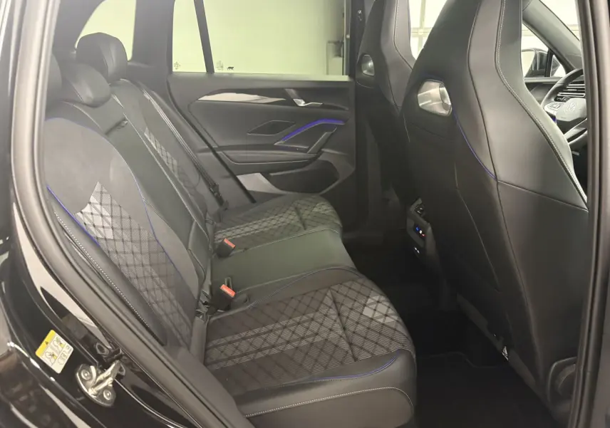 Vue intérieure arrière côté gauche du Volkswagen Tiguan 2025 avec sièges en tissu noir à motifs et surpiqûres bleues.
