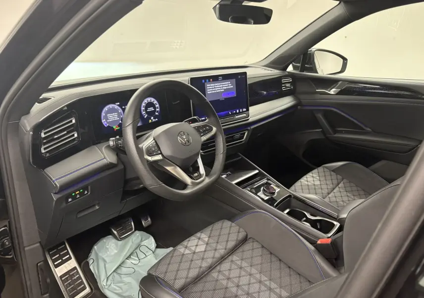 Vue intérieure côté conducteur du Volkswagen Tiguan 2025 avec tableau de bord numérique et sellerie cuir noire à surpiqûres bleues.