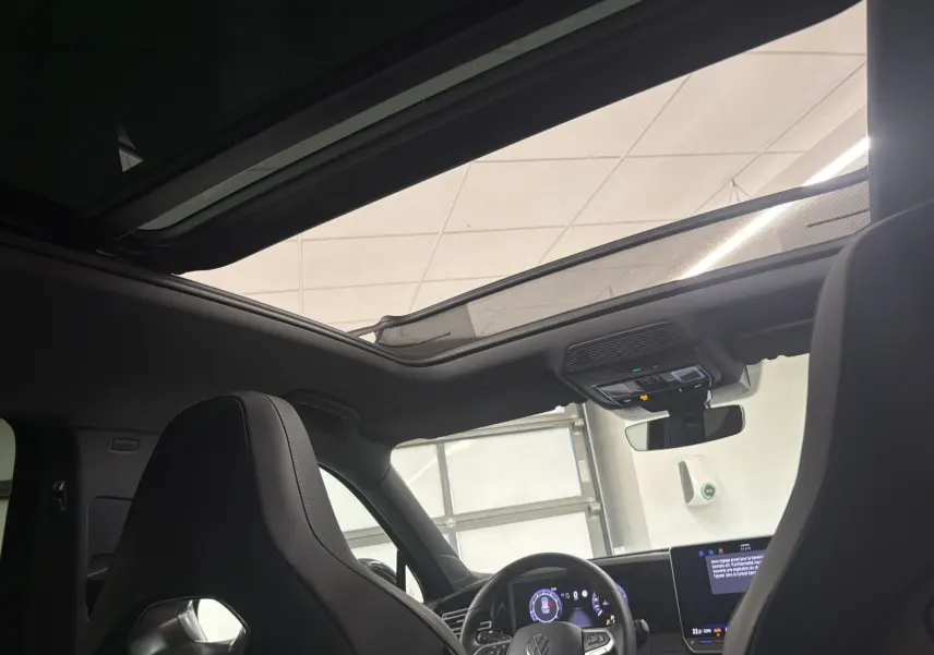 Vue intérieure du Volkswagen Tiguan 2025 avec toit ouvrant panoramique, volant multifonction et sièges avant en cuir noir.