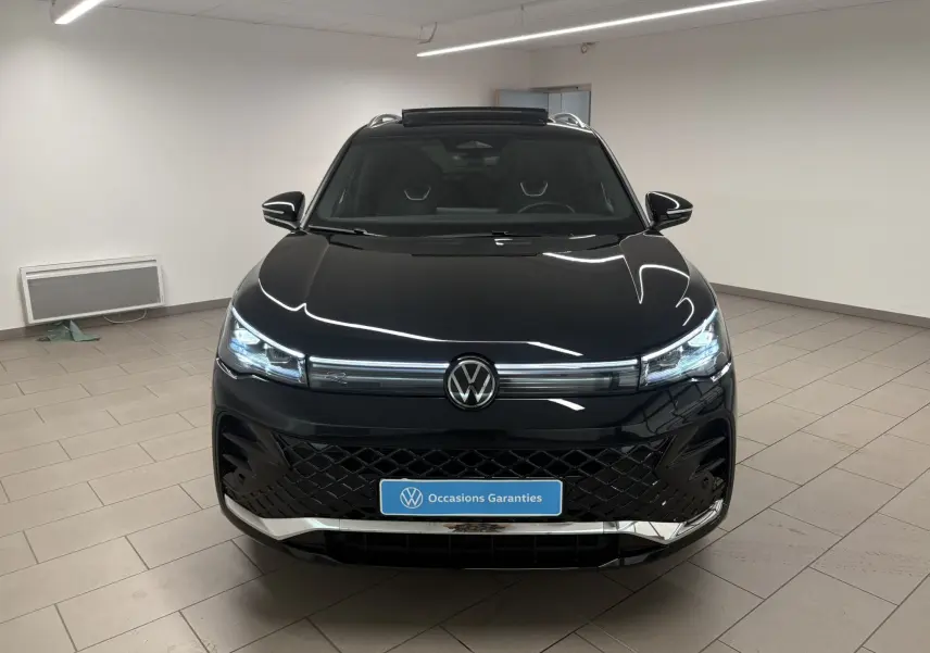 Vue avant d'un Volkswagen Tiguan 2025 noir intense nacré avec toit ouvrant et calandre R-Line dans un showroom.