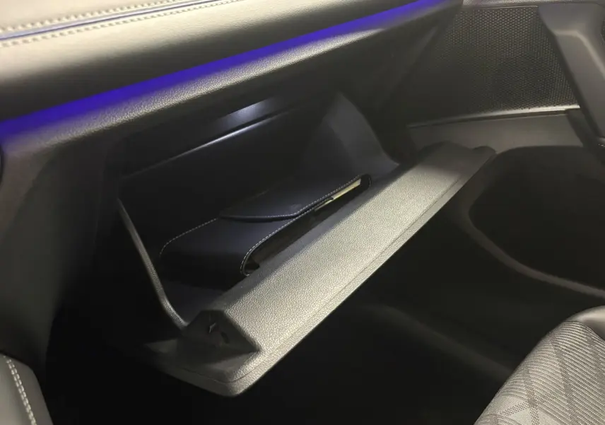 Gros plan sur la boîte à gants ouverte côté passager du Volkswagen Tiguan 2025, intérieur noir avec éclairage bleu subtil.