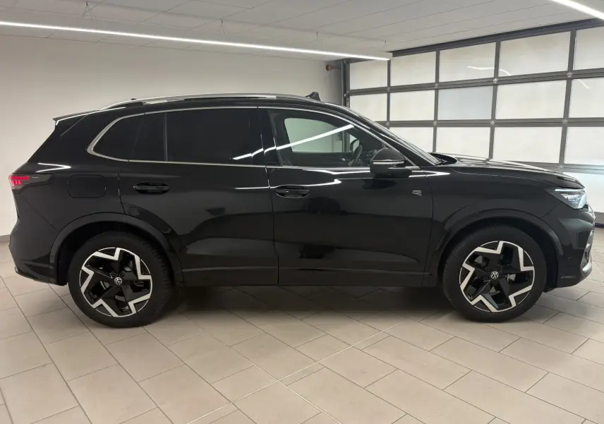 Profil droit du Volkswagen Tiguan 2025 noir intense nacré avec jantes R-Line distinctives et toit ouvrant visible.