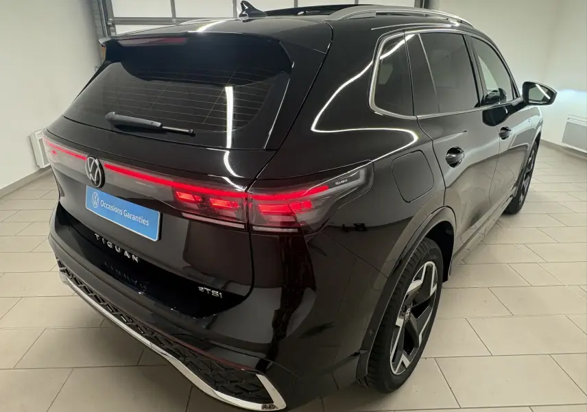 Vue 3/4 arrière droite du Volkswagen Tiguan 2025 noir intense nacré avec feux arrière allumés et toit ouvrant visible.