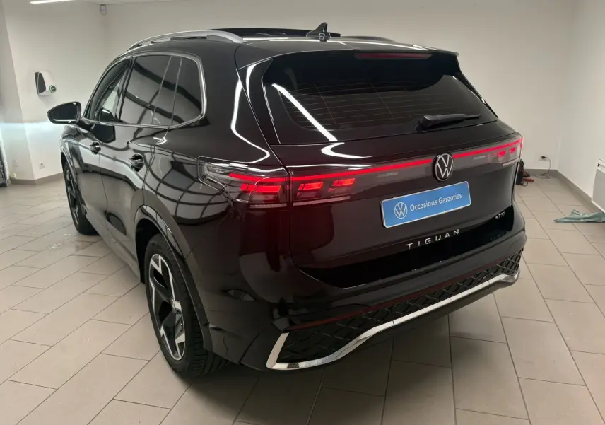 Vue 3/4 arrière gauche du Volkswagen Tiguan 2025 noir intense nacré avec feux arrière LED et toit ouvrant en intérieur showroom.