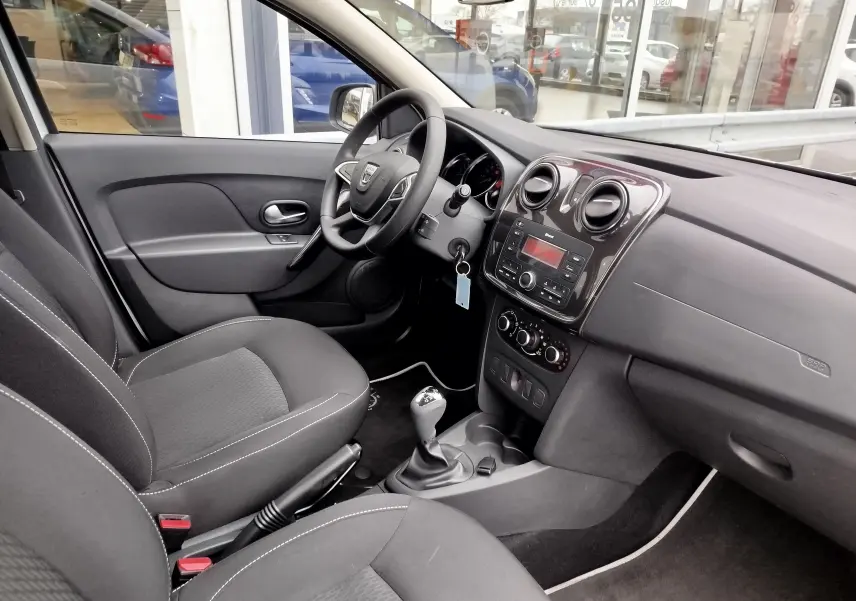 Intérieur avant droit de la Dacia Sandero 2019, sièges tissu gris et tableau de bord avec console centrale noire.
