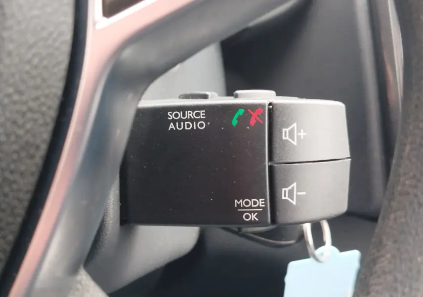Gros plan sur la commande audio au volant de la Dacia Sandero blanc glacier, avec boutons de volume et gestion d'appels.