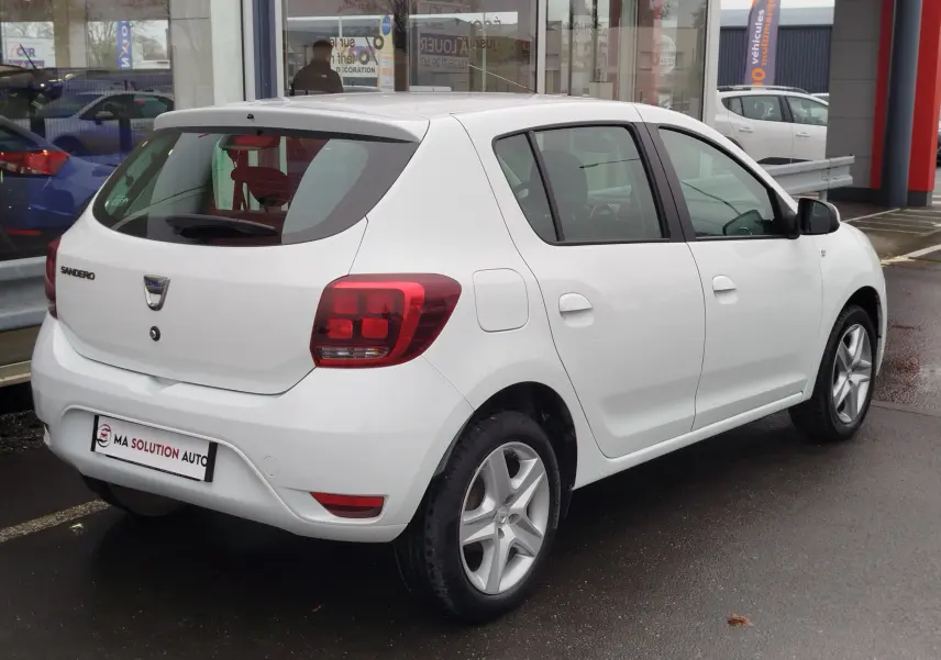 Vue 3/4 arrière droite d'une Dacia Sandero blanc glacier, compacte cinq portes avec jantes alliage et feux arrière rouges.