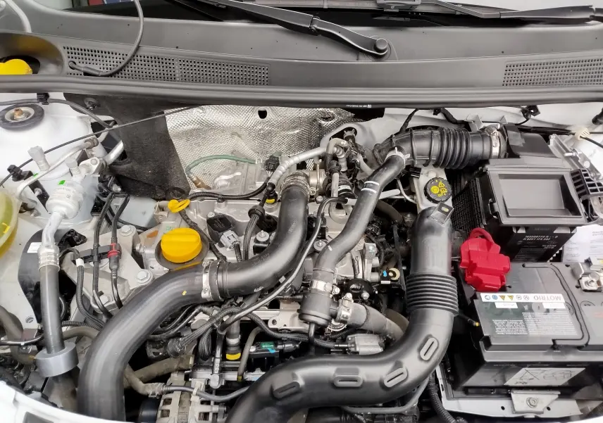 Moteur essence de la Dacia Sandero blanc glacier vu de dessus, avec durites noires et batterie à capuchon rouge visible.