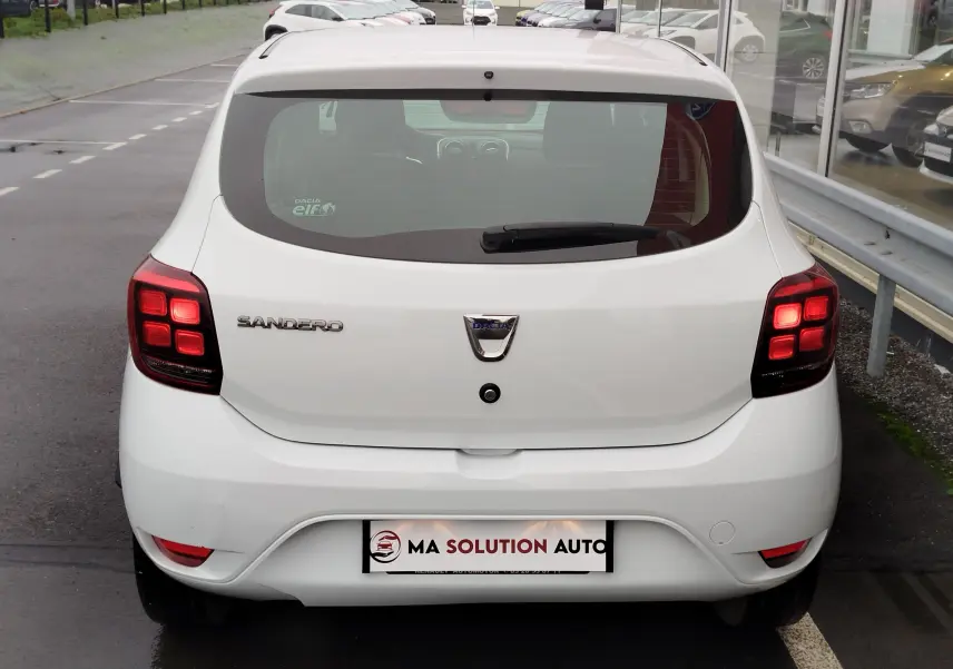 Vue arrière d'une Dacia Sandero blanc glacier de 2019, avec feux arrière allumés et logo bien visible.