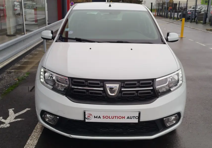 Vue frontale d'une Dacia Sandero blanc glacier de 2019 avec calandre noire et feux LED allumés.
