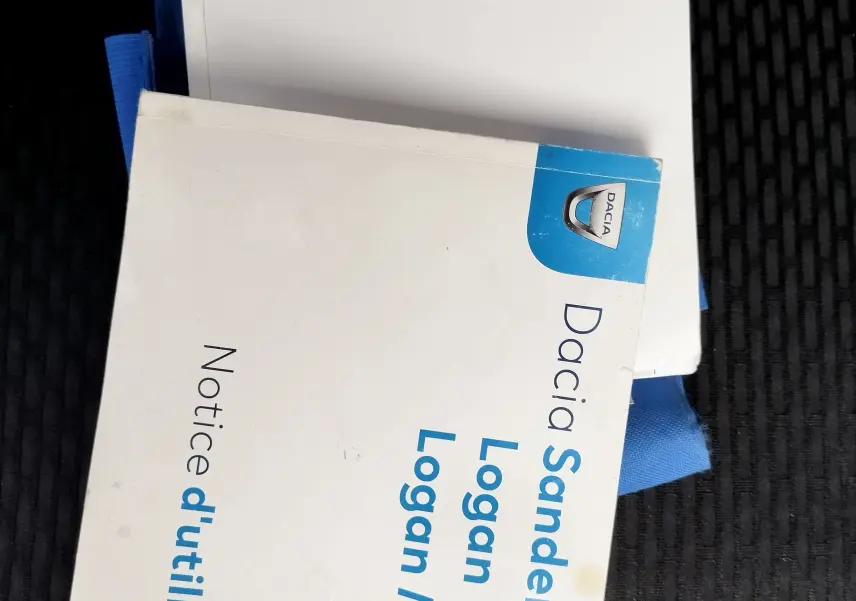 Manuels d'utilisation Dacia Sandero, Logan et Logan MCV posés sur un siège de voiture sombre, vue de dessus.