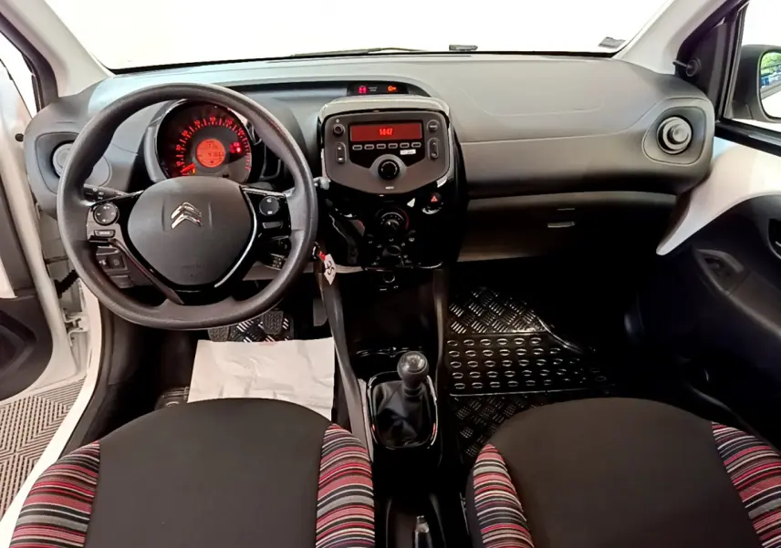 Vue intérieure avant de la Citroën C1 blanche, montrant le tableau de bord, volant et levier de vitesse manuel.