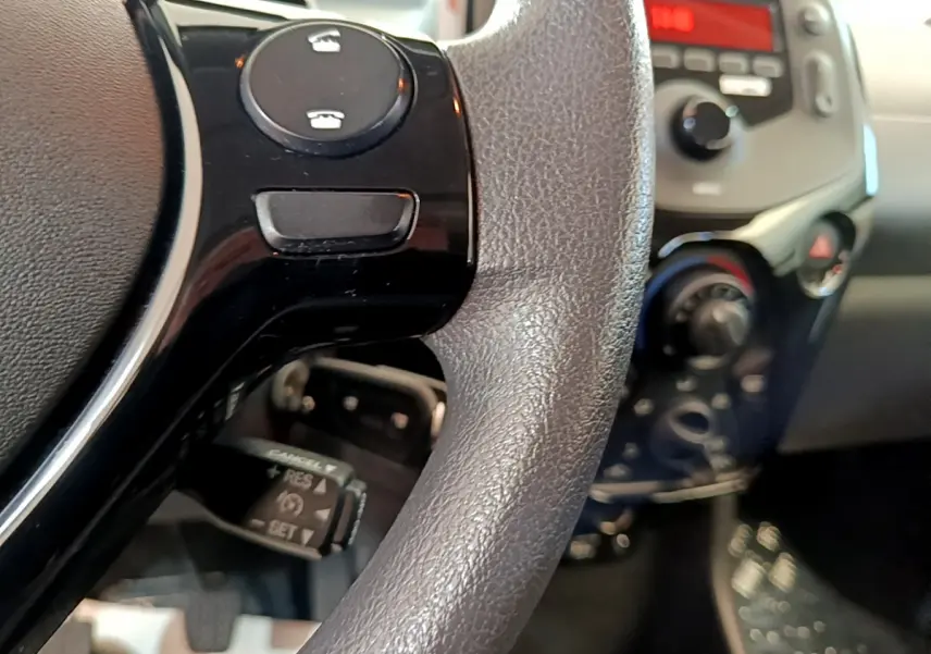 Gros plan sur le volant noir avec commandes intégrées et tableau de bord flou d'une Citroën C1 blanche de 2020.