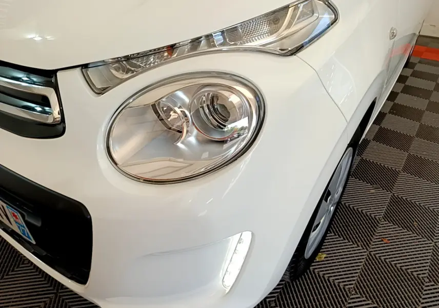 Gros plan sur l'avant droit blanc d'une Citroën C1 2020, mettant en valeur le phare rond et la LED verticale.