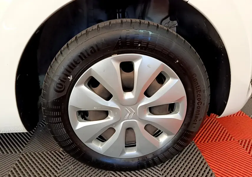 Gros plan sur la roue avant droite blanche d'une Citroën C1 VTi 72 S&S BVM Feel avec enjoliveur argenté.