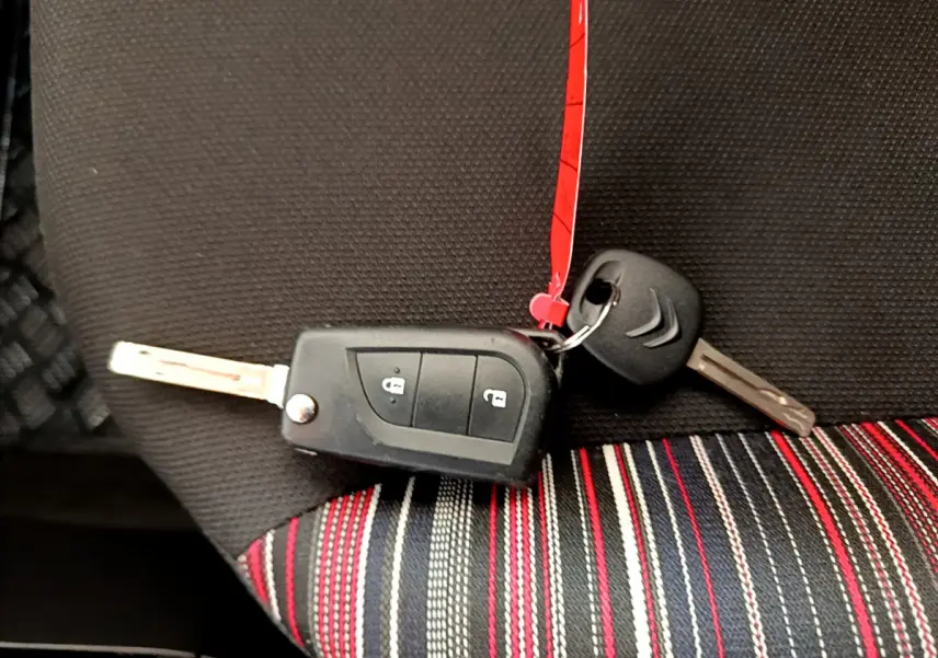 Clé de voiture Citroën posée sur un siège tissu noir à rayures rouges, blanches et grises, intérieur d'une C1 blanche.