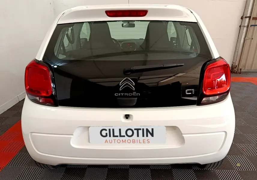 Vue arrière d'une Citroën C1 blanche avec hayon noir brillant et feux arrière rouges dans un garage.