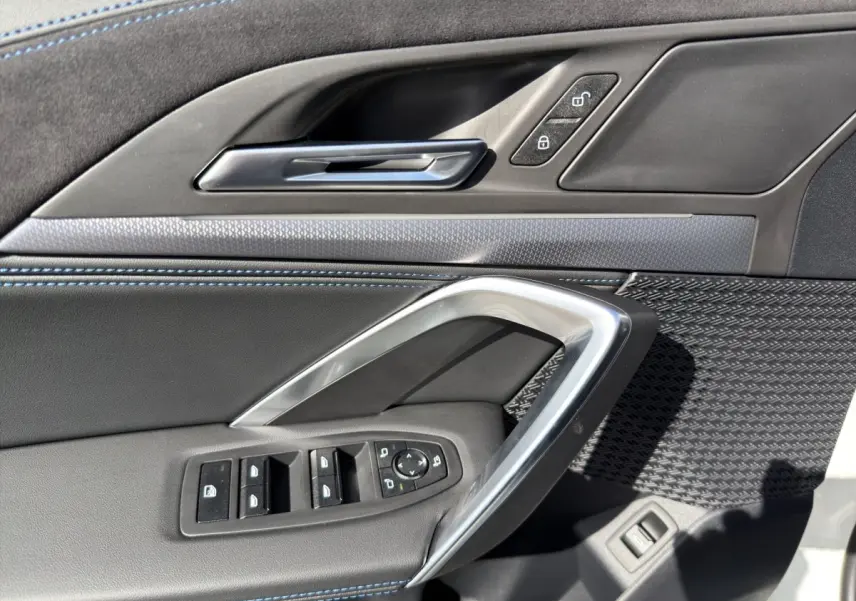 Détail de la porte avant gauche du BMW X1 blanc 2025, avec commandes de vitres et surpiqûres bleues.