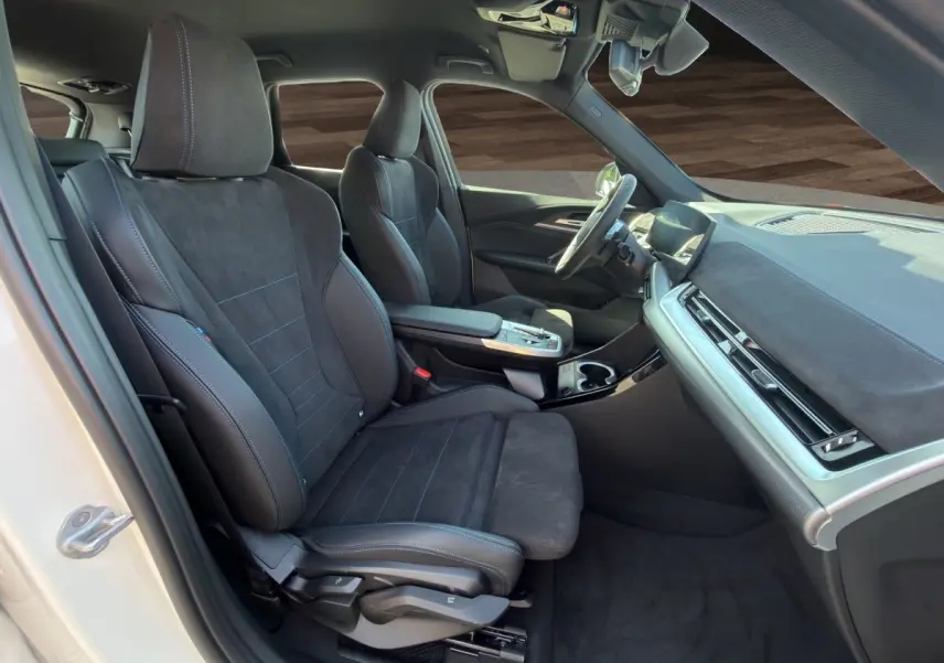 Intérieur avant droit de la BMW X1 blanc 2025, sièges sport noirs avec surpiqûres bleues et tableau de bord moderne.