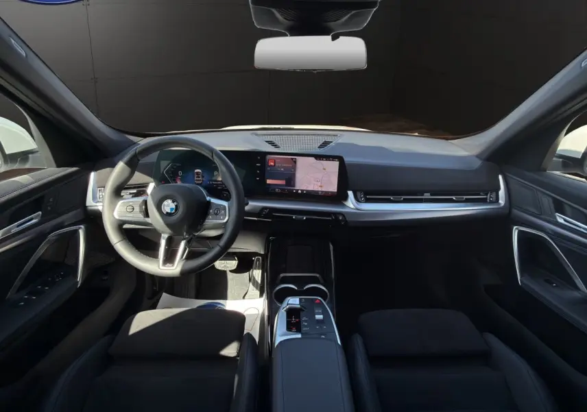 Intérieur noir de la BMW X1 sDrive20d 2025 vu de face, avec tableau de bord numérique et écran tactile central.