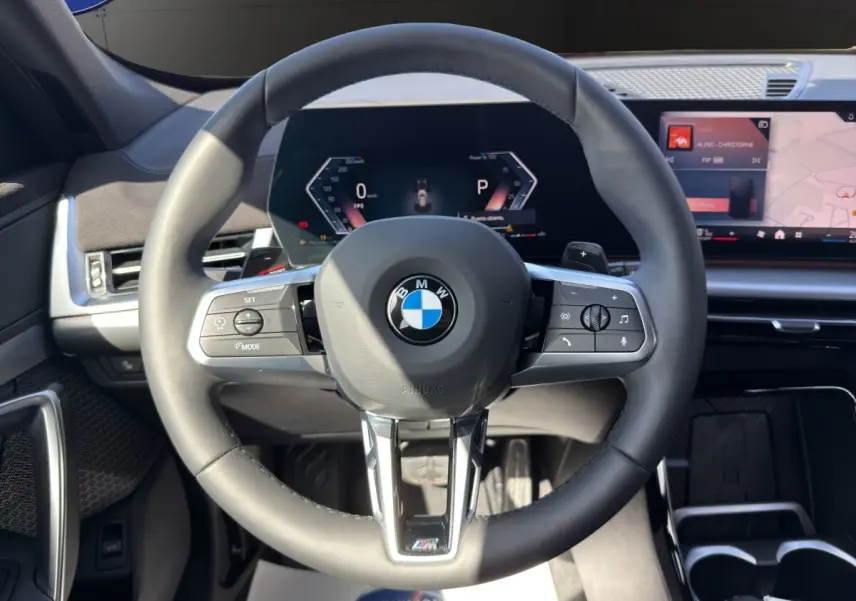 Vue rapprochée du volant noir BMW M Sport avec tableau de bord numérique et écran tactile central.