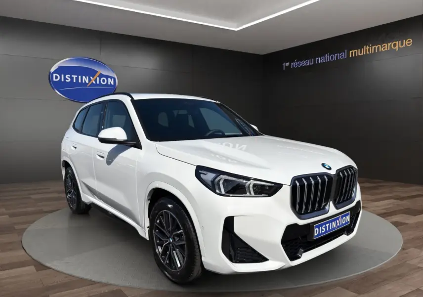 BMW X1 sDrive20d blanc vue 3/4 avant droite avec calandre noire et jantes foncées en showroom